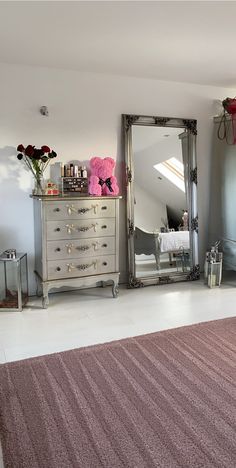 a bedroom with a dresser, mirror and pink flowers on the floor in front of it