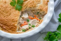 a chicken pot pie in a white dish with a slice cut out and garnished with parsley