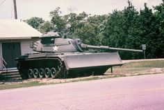 an old tank is parked in front of a small house on the side of the road