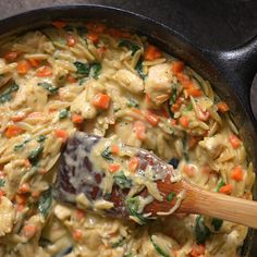 a skillet filled with pasta and vegetables being stirred by a wooden spatula on the stove