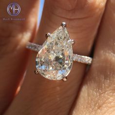 a woman's hand holding an engagement ring with a pear shaped diamond on it