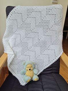 a crocheted blanket with a teddy bear sitting on the chair next to it