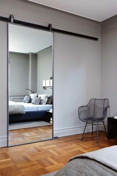 a bedroom with a bed, chair and large mirror on the wall in front of it