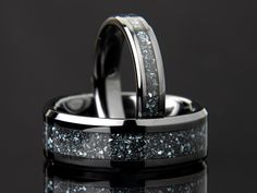 two wedding rings with blue and white glitters on each one, against a black background