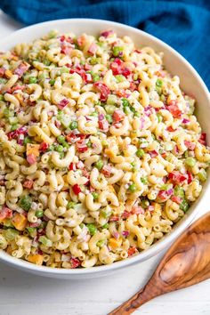 a white bowl filled with pasta salad next to a wooden spoon on top of a table