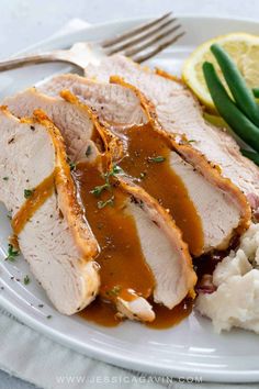 sliced pork with gravy, mashed potatoes and green beans on a white plate