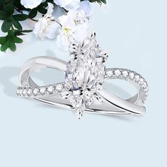 a pear shaped diamond ring with white flowers in the background