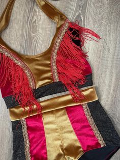 a women's swimsuit with red and gold fringes on the bottom, sitting on a wooden floor