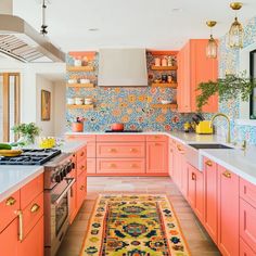 an orange kitchen with pink cabinets and rug on the floor in front of the stove