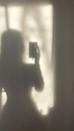 a blurry image of a person taking a photo with a cell phone in front of a window