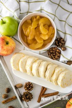 apples, cinnamon and nuts are arranged on a white platter next to a bowl of apple slices