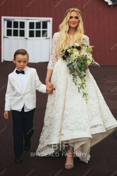 a woman in a white dress holding the hand of a young boy wearing a tuxedo