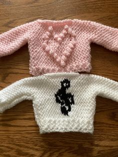 two knitted sweaters sitting on top of a wooden table