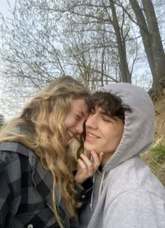 two people standing next to each other with trees in the background and one person talking on a cell phone