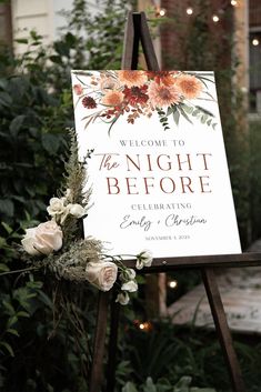 a welcome sign with flowers on it in front of some bushes and lights at night