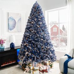 a blue christmas tree in a living room with presents under it and a fire place