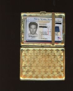 a new york state id card in a gold metal case on a black surface with the image of a man's face