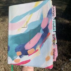 a person holding up a notebook covered in colorful paint