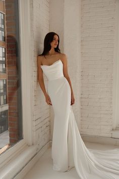 a woman standing in front of a window wearing a white dress and posing for the camera