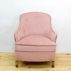 a pink chair sitting on top of a hard wood floor next to a white wall