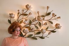 a woman standing in front of a wall sculpture with flowers on it's side