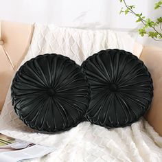 two black round pillows sitting on top of a bed next to a book and plant