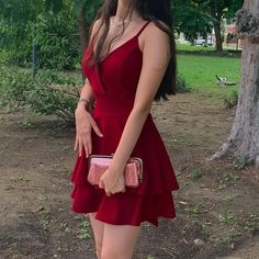 a woman in a red dress is holding a pink purse and posing for the camera