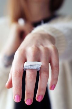 a woman's hand with a ring on it and pink nail polish holding something in her other hand