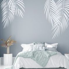 a white bed sitting under a palm leaf wall decal