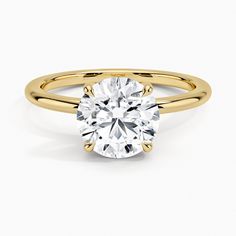 a yellow gold engagement ring with a round cut diamond in the center, on a white background