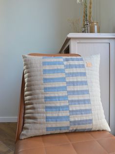 a blue and white striped pillow sitting on top of a brown leather chair next to a plant