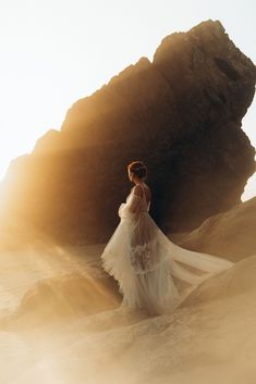 a woman standing in the sand with her dress blowing in the wind, looking back