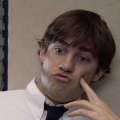 a young man in a white shirt and tie poses for the camera with his finger on his nose