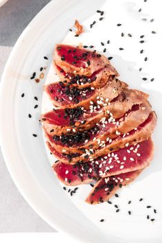 a white plate topped with sliced meat covered in sesame seeds and black pepper flakes