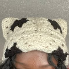 a woman wearing a crocheted hat with black and white cats on the top