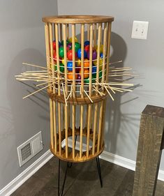 a wooden tower with balls in it and sticks sticking out of the top, against a gray wall