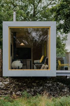 a dog is standing in the window of a small house that's surrounded by grass and trees