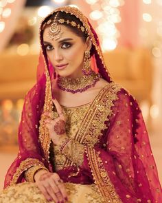 a woman in a red and gold bridal outfit posing for the camera with her hand on her hip