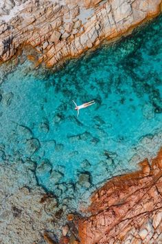 an aerial view of a person swimming in clear blue water near rocky coastlines and cliffs