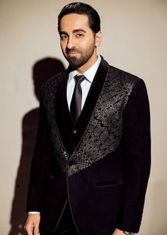 A adorned black tuxedo featuring a black velvet placket and intricate embroidery embellished with metallic beads across the chest area. Luxury Black Embellished Blazer, Designer Black Embellished Blazer, Designer Embellished Black Blazer, Elegant Party Blazer With Intricate Embroidery, Elegant Embellished Evening Bandhgala, Velvet Party Suits For Winter, Velvet Tuxedo For Winter Party, Winter Velvet Party Suits, Black Velvet Party Blazer