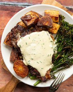 a plate with potatoes, broccoli and gravy on it next to a fork