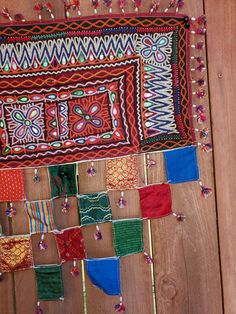 several colorful pieces of cloth are hanging on a wooden wall with beads and tassels