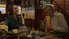 a man and woman sitting at a table with food in front of them, talking to each other