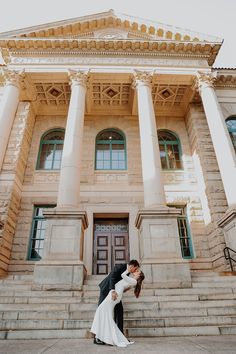 a bride and groom kissing in front of a large building with columns on the side