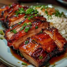 some meat and rice on a plate with chopsticks next to it in the foreground