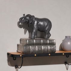 an elephant figurine on top of two books and a vase sitting on the shelf