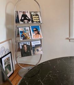 a magazine rack with magazines on it next to a round table and framed pictures in the corner