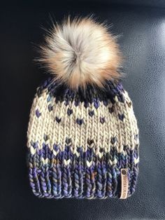 a knitted beanie with a pom - pom on the top, sitting on a black surface