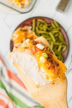 a wooden spoon holding up a piece of food with green beans and cheese on it