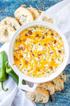 a white bowl filled with cheese and bread on top of a blue table next to green peppers